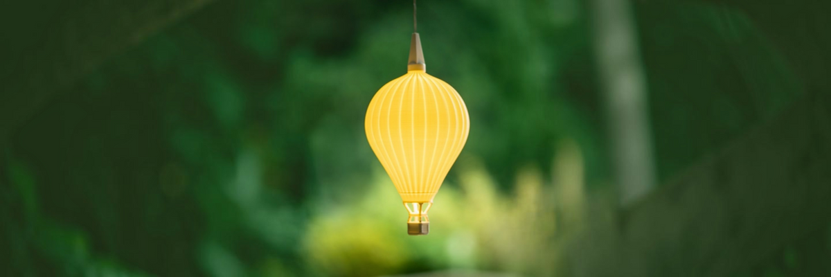 Leuchtender gelber Heißluftballon Lampenschirm von Benago Lights schwebt an einem Kabel vor unscharfem grünem Garten