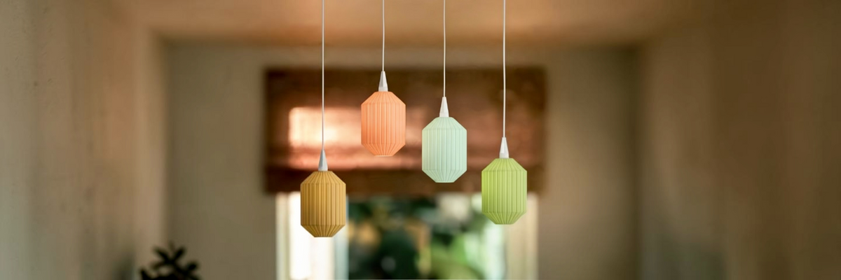 Vier Konic Lampenschirme von Benago Lights in Senfgelb, Koralle, Mint und Lindgrün hängen in unterschiedlicher Höhe vor einem hellen Fenster