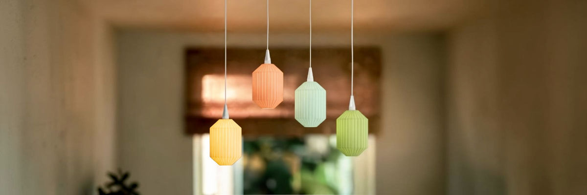 Vier Konic Lampenschirme von Benago Lights in Senfgelb, Koralle, Mint und Lindgrün hängen in unterschiedlicher Höhe vor einem hellen Fenster