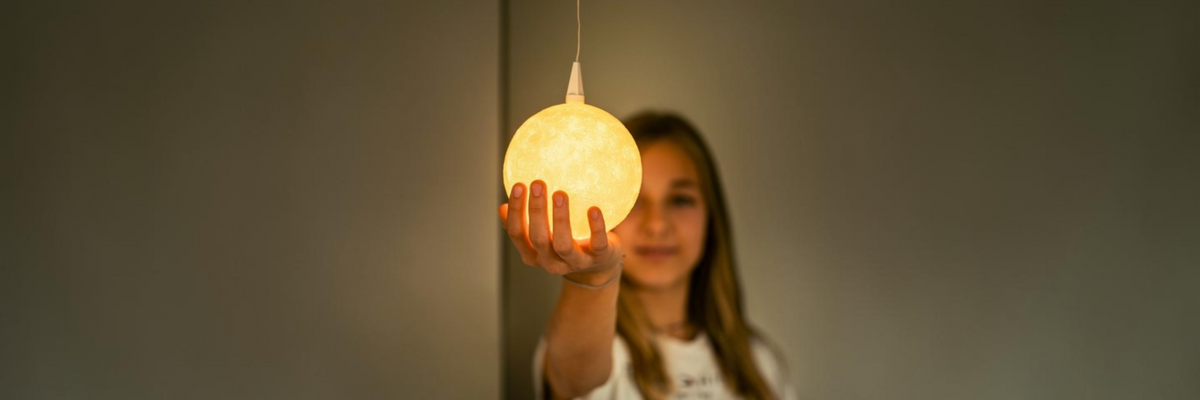 Mädchen hält einen leuchtenden The Moon Lampenschirm von Benago Lights in der ausgestreckten Hand