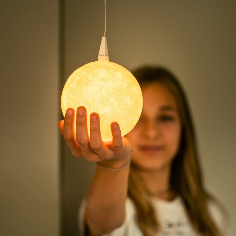 Warm leuchtender Lampenschirm The Moon von Benago Lights hängt an einem Kabel, eine Hand berührt den Schirm